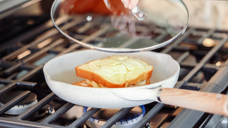 Within the sleek setting of a modern white kitchen, banana slices and brioche bread sizzle on a non-stick pan over a gas stove, setting the stage for an enticing grilled peanut butter banana sandwich.の写真素材