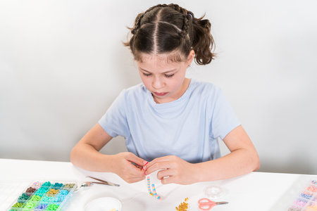 Little girl enjoys crafting colorful bracelets with vibrant clay beads set.の写真素材