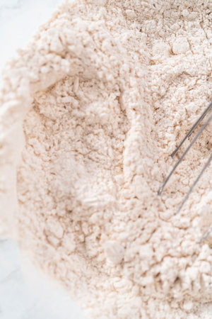 Mixing dry ingredients in a large glass mixing bowl to bake eggnog cookies with a chocolate gingerbread man.の写真素材