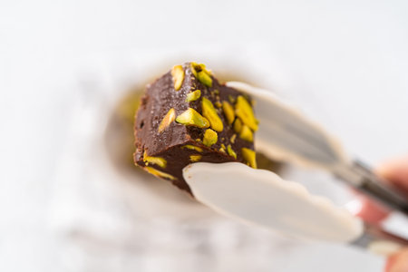 Holding homemade chocolate pistachio fudge square piece with kitchen tongs.