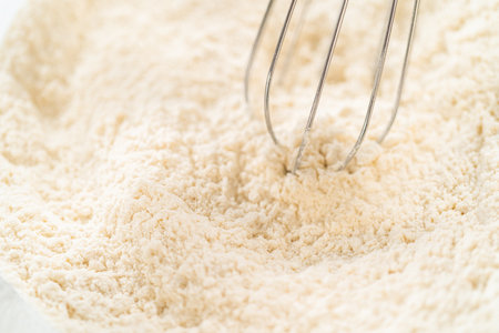 Mixing dry ingredients with a hand whisk in a glass mixing bowl to bake no-yeast cinnamon roll cupcakes.の写真素材