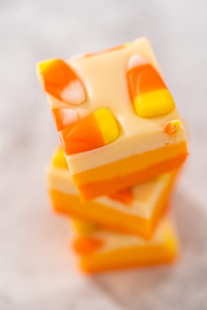 Homemade candy corn fudge square pieces stacked on a kitchen counter.