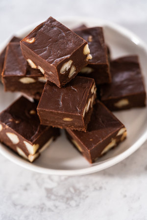 Homemade chocolate macadamia fudge square pieces on a white plate.の写真素材