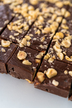 Cutting chocolate hazelnut fudge with a large kitchen knife into square pieces on a white cutting...