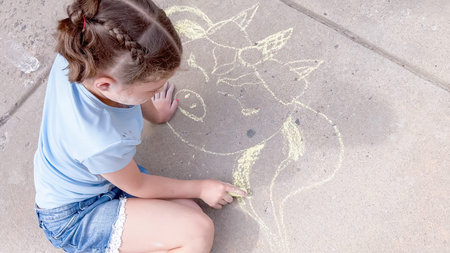 Little girl drawing chalk art on a suburban driveway on a summer day.の写真素材