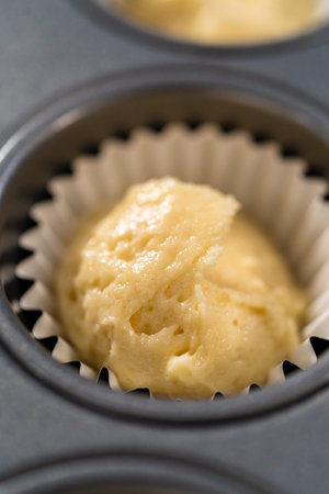 Scooping cupcake batter with dough scoop into a baking cupcake pan with liners to bake mini vanilla...