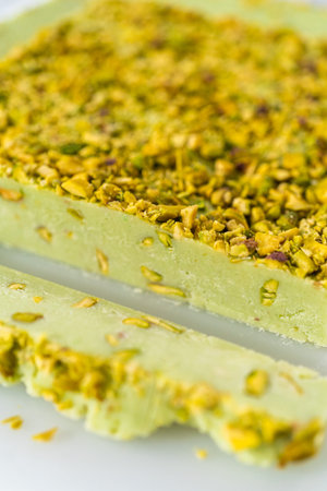 Cutting pistachio fudge into square pieces on a white cutting board.