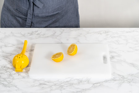 Zesting and juicing fresh lemon on a white cutting board.の写真素材