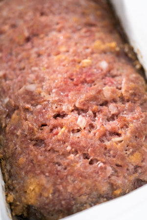 Glazing classic meatloaf with sweet glaze in a loaf pan lined with parchment paper.
