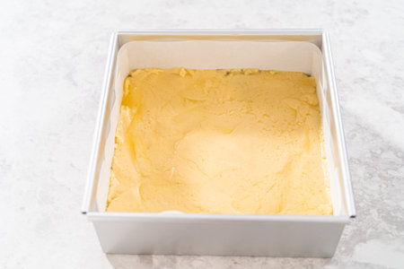 Filling square cheesecake pan lined with parchment paper with fudge mixture to prepare candy cane fudge.の写真素材