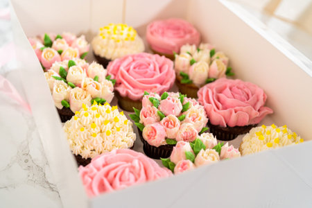 Encased in a pristine white paper cupcake box, each gourmet cupcake is a work of art, adorned with buttercream frosting flowers beautifully designed to resemble vibrant roses and tulips.の写真素材