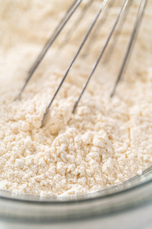 Mixing dry ingredients with a hand whisk in a glass mixing bowl to bake white chocolate macadamia nut.の写真素材