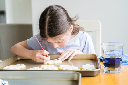 A heartwarming scene of a little girl carefully writing Sorry on sugar cookies with food coloring, the cookies beautifully flooded with white royal icing.の写真素材