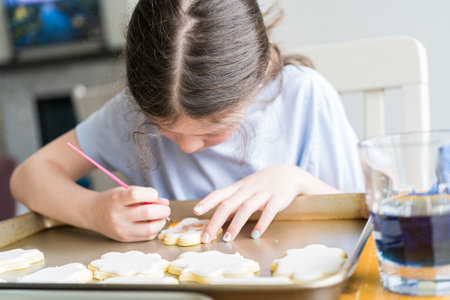 A heartwarming scene of a little girl carefully writing Sorry on sugar cookies with food coloring, the cookies beautifully flooded with white royal icing.の写真素材