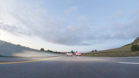 As the sun sets, driving on HWY 101 near Pismo Beach, California becomes a captivating experience with the sky painted in shades of orange and pink, casting a warm glow over the coastal landscape.の写真素材