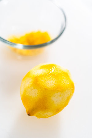 Zesting and juicing fresh lemon on a white cutting board.の写真素材
