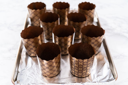 Scooping bread dough into paper liners to bake mini Easter bread kulich.