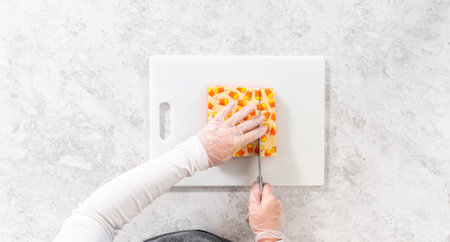 Flat lay. Cutting candy corn fudge into square pieces on a white cutting board.の写真素材