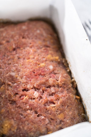 Glazing classic meatloaf with sweet glaze in a loaf pan lined with parchment paper.の写真素材