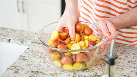 In a sleek, modern kitchen, a young man attentively prepares dinner. His current task involves carefully seasoning small rainbow potatoes in a glass bowl, promising a flavorful meal ahead.の写真素材
