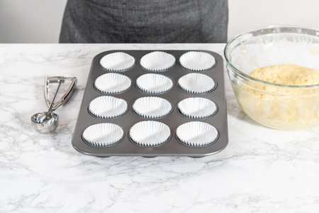 Scooping cupcake dough with a dough scoop into foil liners to bake lemon cupcakes.