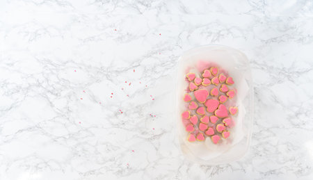 Flat lay. Storing heart-shaped sugar cookies with pink and white royal icing in a large plastic...