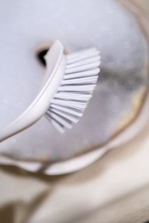 Scrubbing dirty aluminum bundt cake pan with kitchen scrub brush in a kitchen sink.の写真素材