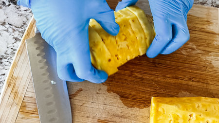 Wearing blue disposable gloves for hygiene, someone is skillfully slicing into a juicy organic watermelon on a wooden cutting board, set on a clean kitchen countertop.の写真素材