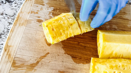 Wearing blue disposable gloves for hygiene, someone is skillfully slicing into a juicy organic watermelon on a wooden cutting board, set on a clean kitchen countertop.の写真素材
