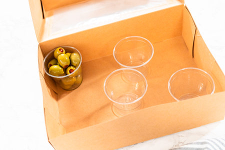 In the process of assembling, a woman expertly curates this charcuterie box, showcasing sliced meat,...