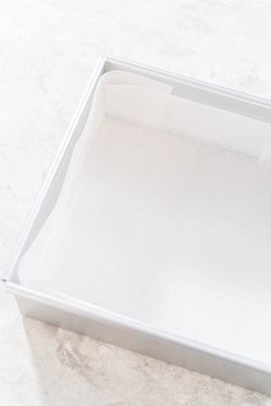 Lining square cheesecake pan with parchment paper sheet to prepare eggnog fudge.の写真素材