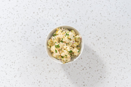 Flat lay. Serving potato salad garnished with fresh parsley in a white ceramic bowl.の写真素材