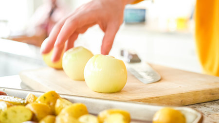 In the welcoming setting of a modern kitchen, a young man continues his dinner preparation process. Hes currently involved in slicing yellow onions into rings, prepping them for grilling on an outdoor grill, a crucial step in creating a flavorful meal.の写真素材