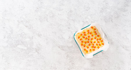 Flat lay. Pouring fudge mixture into the square glass baking pan lined with parchment paper to prepare candy corn fudge.の写真素材