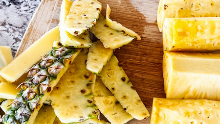 Wearing blue disposable gloves for hygiene, someone is skillfully slicing into a juicy organic watermelon on a wooden cutting board, set on a clean kitchen countertop.の写真素材