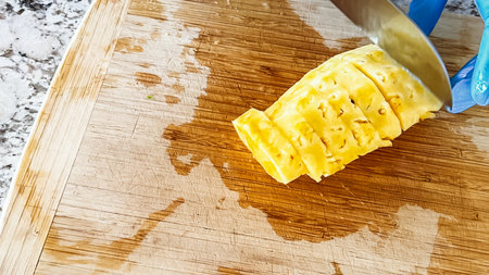 Wearing blue disposable gloves for hygiene, someone is skillfully slicing into a juicy organic watermelon on a wooden cutting board, set on a clean kitchen countertop.の写真素材