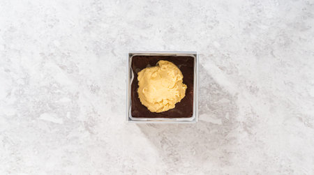 Flat lay. Filling square cheesecake pan lined with parchment paper with fudge mixture to prepare...
