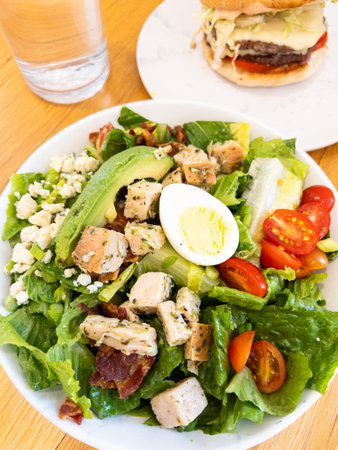 Grilled herb chicken, crisp bacon, boiled eggs, and cherry tomatoes on a bed of fresh lettuce with crumbled cheeseの写真素材