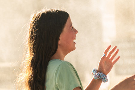 A joyful young girl gleefully gets soaked in refreshing water mist during a hot summer day.の写真素材