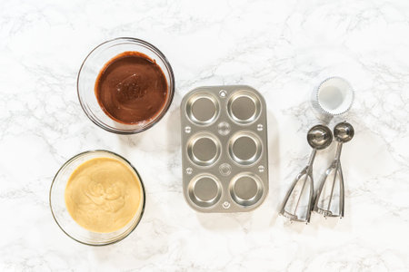 Flat lay. Cupcake foil liners are being meticulously filled with both chocolate and vanilla batter,...
