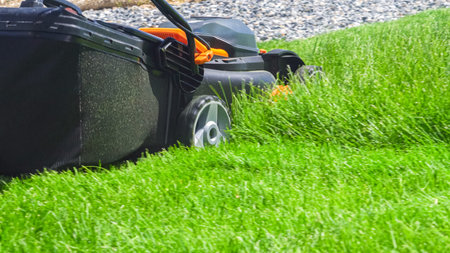 At a residential suburban house, a lush green lawn is meticulously mowed using an electric lawn...