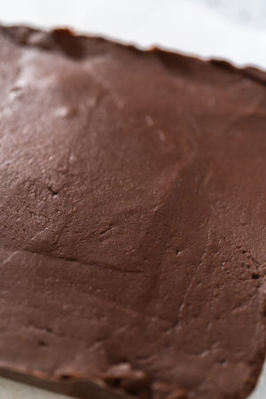 Cutting plain homemade fudge into small pieces on a white cutting board.