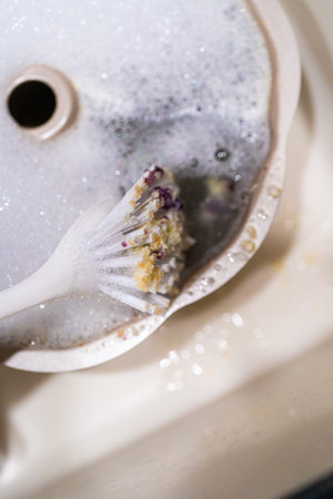 Scrubbing dirty aluminum bundt cake pan with kitchen scrub brush in a kitchen sink.の写真素材