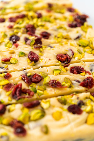 Cutting cranberry pistachio fudge with a large kitchen knife into square pieces on a white cutting board.の写真素材