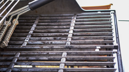 In an outdoor setting, the two-burner gas grill is receiving careful attention before the cooking begins. The grill is meticulously cleaned with a specialized grill brush, ensuring an optimal and hygienic surface for the forthcoming dinner preparations.の写真素材