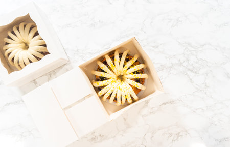 Flat lay. The freshly baked bundt cakes are carefully nestled into white paper boxes, preparing them...