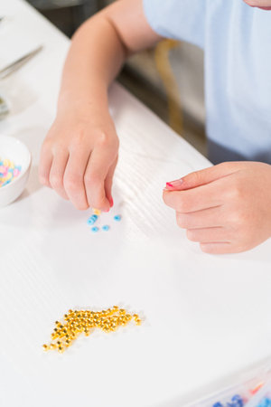 Little girl enjoys crafting colorful bracelets with vibrant clay beads set.の写真素材