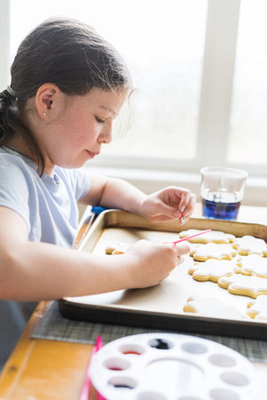 A heartwarming scene of a little girl carefully writing Sorry on sugar cookies with food coloring, the cookies beautifully flooded with white royal icing.の写真素材