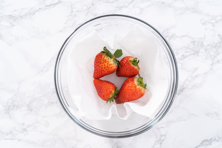 Bright red strawberries, interspersed with signs of mold, rest in a glass bowl lined with a paper towel on a white napkin, indicating improper storage techniques.の写真素材