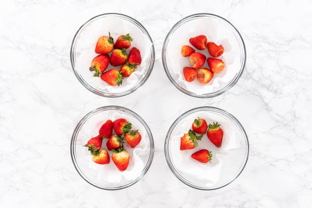 Freshly washed and dried strawberries are carefully arranged in a glass bowl lined with paper towel, ready for snacking or further use.の写真素材